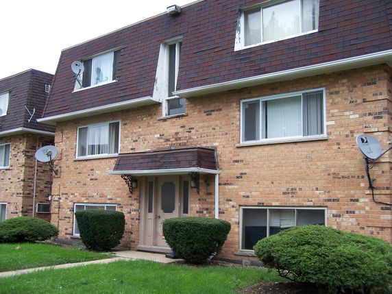 Front view of a residential building with brick facade and brown shingle roof.