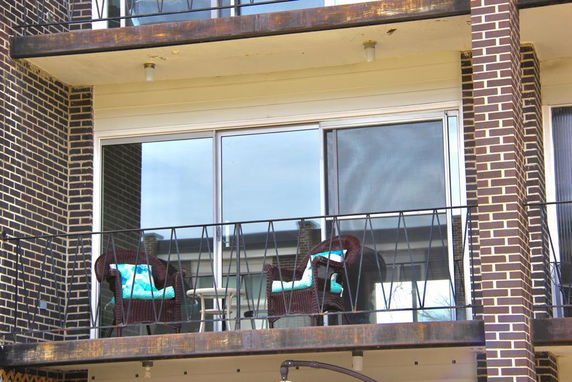 Front view of a building with a balcony featuring chairs and a table.