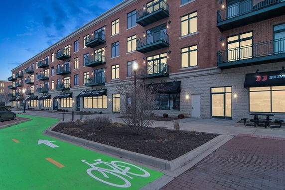 Front view of a multi-story brick building with balconies and ground floor retail spaces.