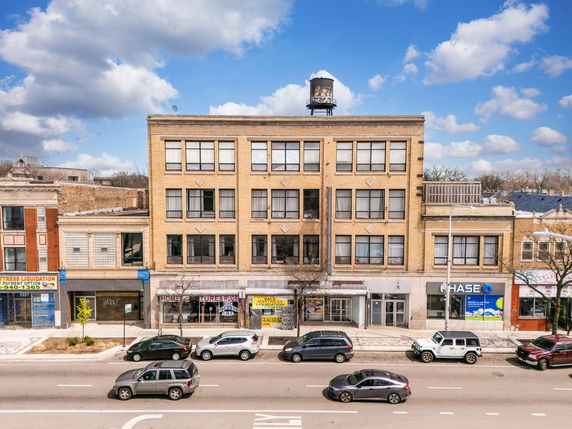 Front view of a multi-story commercial building with various storefronts on the ground floor and a water tower on the roof.