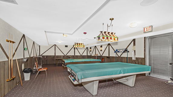 Indoor recreation area with billiards tables and cue sticks.