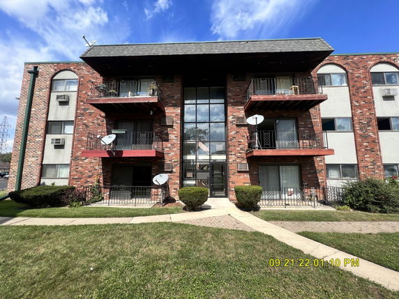 Front view of a multi-story apartment building with balconies and a brick facade.