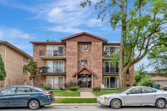 Front view of a three-story brick apartment building with balconies.