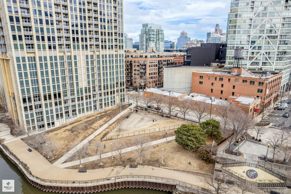 View of tall modern buildings with large windows, adjacent to a waterway and surrounded by trees and pathways.