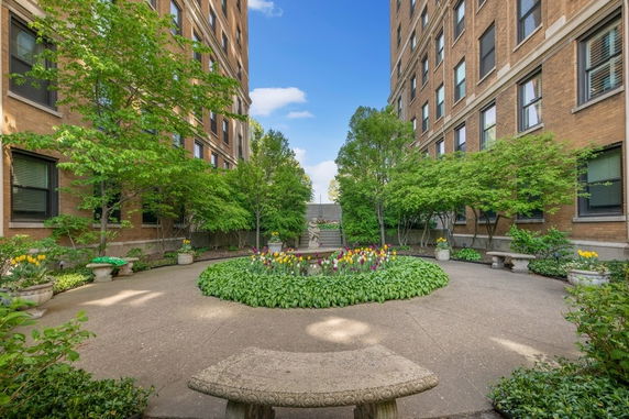 View of a courtyard area between two brick buildings with greenery and a circular flower bed.