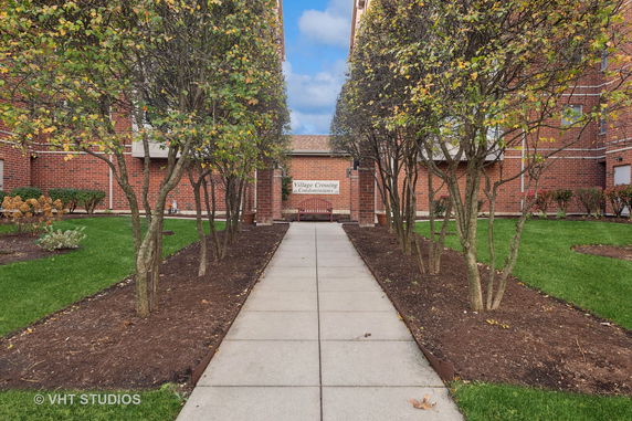 Front view of a multi-story condominium building with trees and walkway leading to entrance.