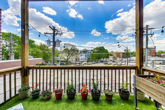 View from a wooden balcony overlooking a street and residential area with planters on the railing.