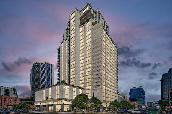 Front view of a modern multi-story building with illuminated windows at dusk.