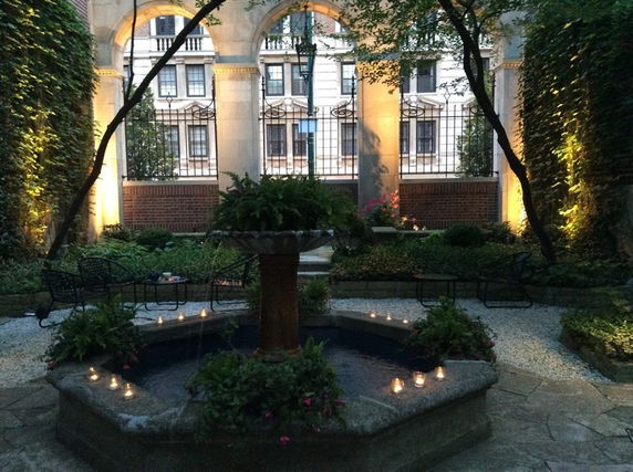 Outdoor garden area with a central fountain, surrounded by greenery and lit with small candles.