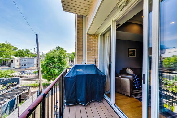 View from a balcony with a grill overlooking nearby buildings and greenery.