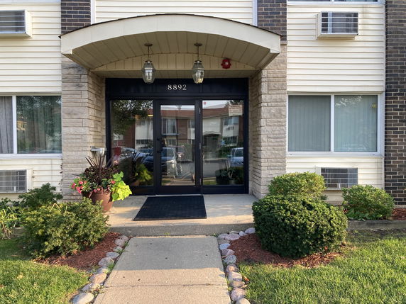 Front view of a building with a glass entrance door and decorative plants.