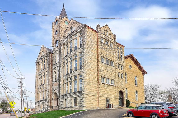 Front view of a large, multi-story stone building with a prominent tower and arched windows.