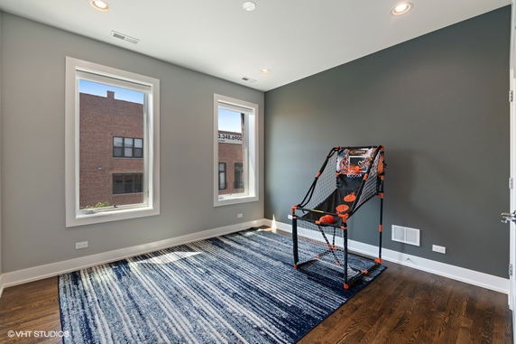 Room with two large windows, gray walls, wooden floor, and an indoor basketball shooting game.