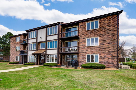 Front view of a three-story brick apartment building with balconies.