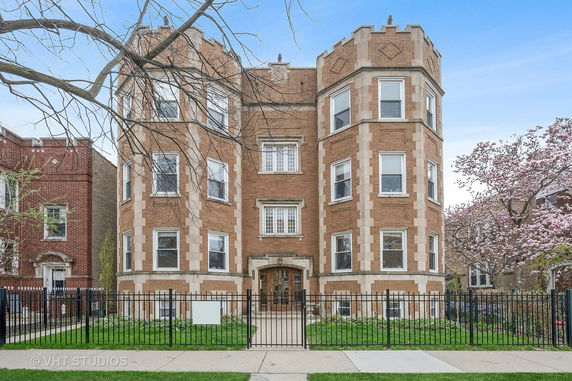 Front view of a multi-story brick building with decorative stone elements and a gated entrance.