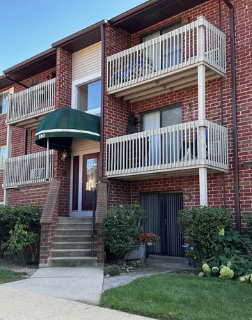 Front view of a two-story red brick apartment building with balconies and a green awning over the entrance.