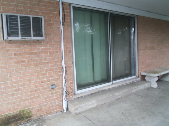 Front view of a brick building with a glass sliding door and a window air conditioning unit.