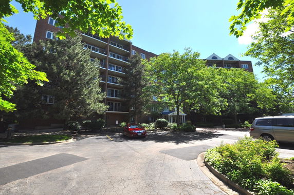 Front view of a multistory apartment building with balconies and surrounded by trees.