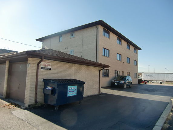 Front view of a three-story brick building with a parking area and garbage bin.