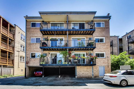 Front view of a multi-story residential building with balconies and a parking area below.