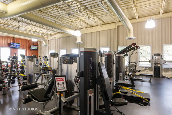 Indoor gym area with various exercise equipment and large ventilation ducts on the ceiling.