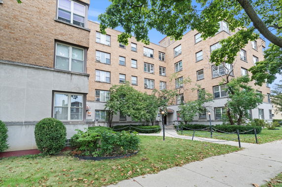 Front view of a multi-story brick building with multiple windows and a landscaped entrance.