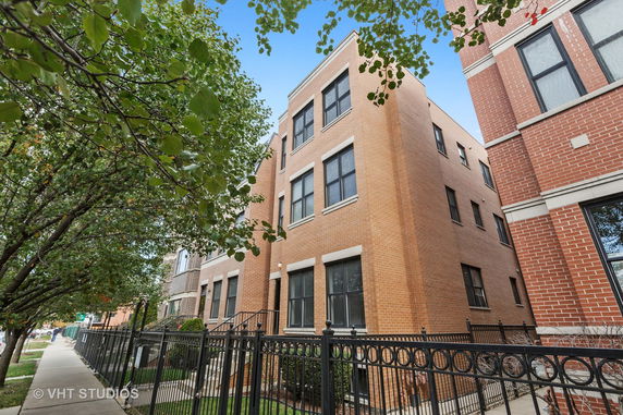 Front view of a multi-story brick building with black framed windows and a fenced entrance.