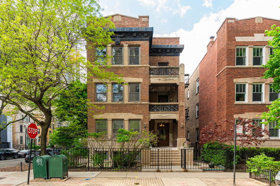 Front view of a three-story brick building with balconies and a gated entrance.