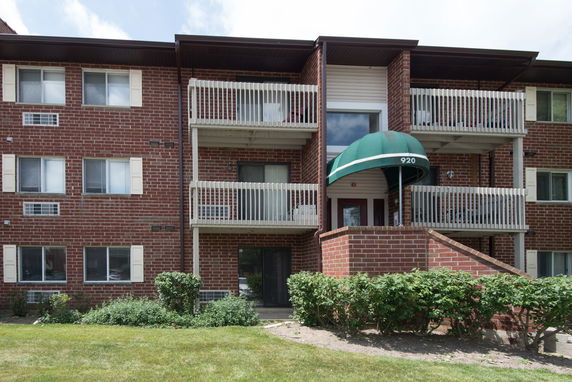 Front view of a brick apartment building with balconies and a green canopy over the entrance.