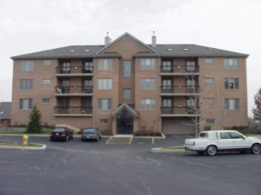 Front view of a multi-story residential building with multiple balconies and parked cars in front.