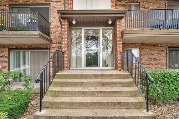 Front view of a brick apartment building with stairs leading to the entrance.