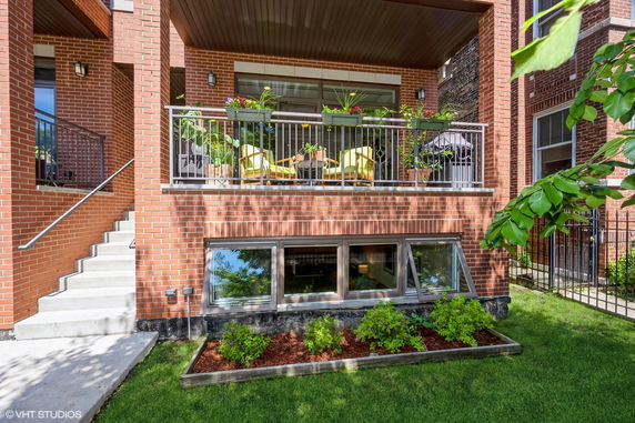 Front view of a brick building with a balcony featuring outdoor seating and plants.