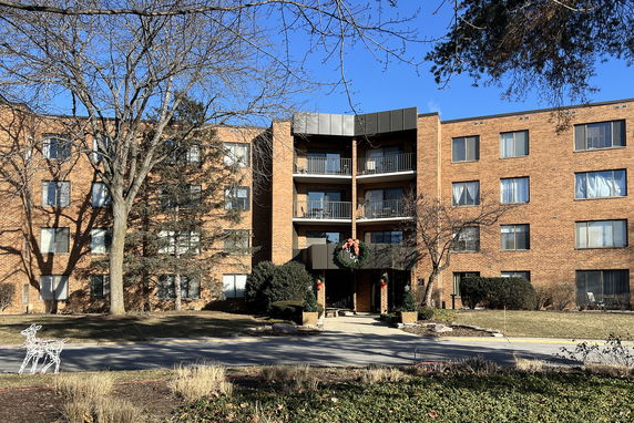 Front view of a multi-story brick apartment building with balconies and a decorated entrance.