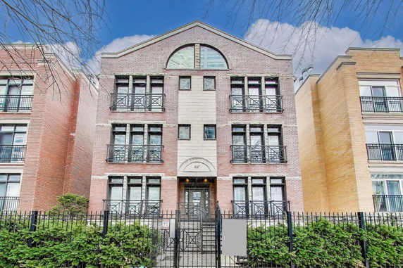 Front view of a multi-story brick apartment building with balconies and central entrance.