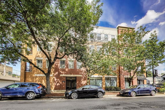Front view of a multi-story brick building with cars parked in front.