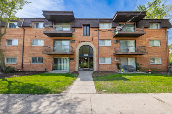 Front view of a three-story brick apartment building with balconies.