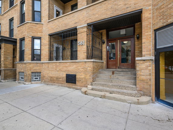Front view of a brick apartment building with stairs leading to the entrance.