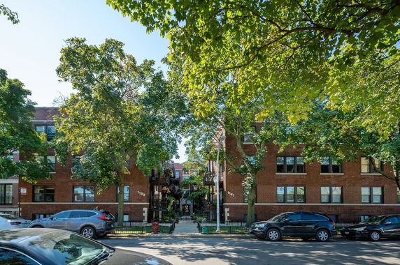 Front view of a multi-story brick building with trees and parked cars in front.