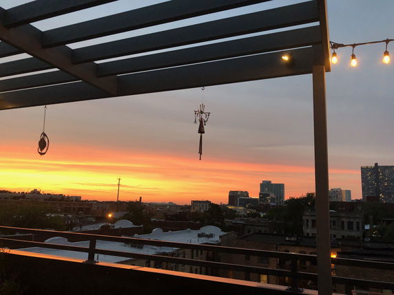 Wide angle view of buildings and sunset from a rooftop patio.