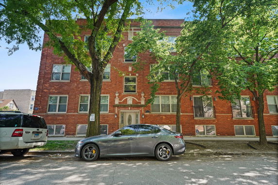 Front view of a brick apartment building with trees and parked cars.