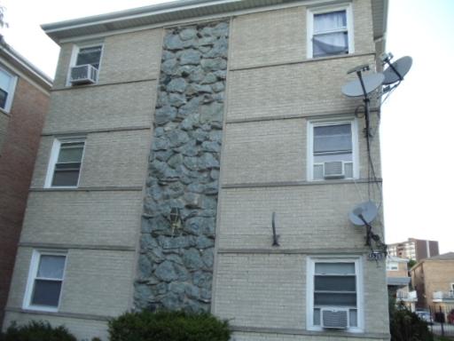 Front view of a three-story apartment building with brick facade and stone details.