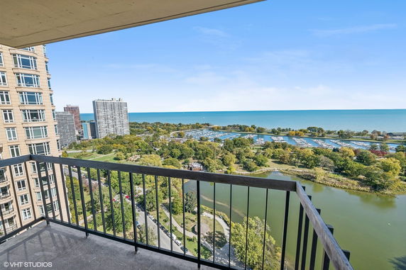 Panoramic view from a balcony showing high-rise buildings, greenery, a marina, and a large body of water.