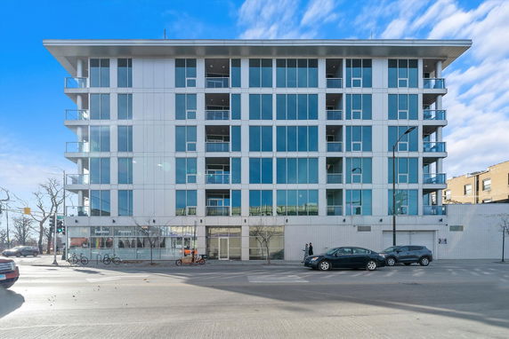 Front view of a modern multi-story building with large glass windows and balconies.