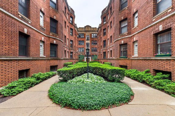 Front view of a multi-story brick apartment building with green landscaping.
