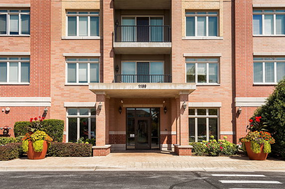 Front view of a multi-story brick building with balconies and large potted plants.