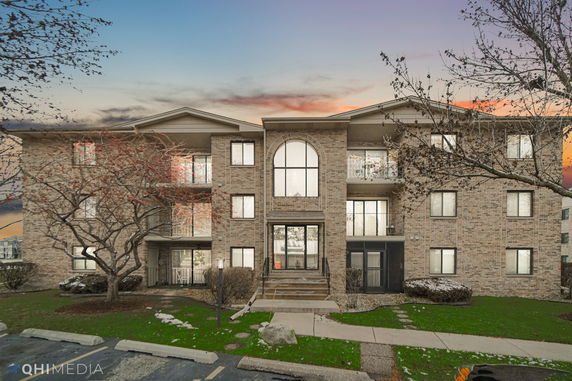 Front view of a multi-story brick apartment building with large windows and a central entrance.