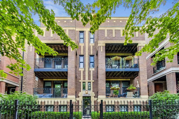 Front view of a multi-story brick building with balconies and a gated entrance.