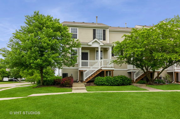 Front view of a two-story house with steps leading to the entrance and surrounded by trees.