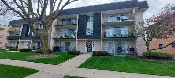 Front view of a three-story apartment building with balconies and a central entrance.