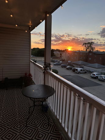 View from a balcony with string lights showing a sunset over a parking area.